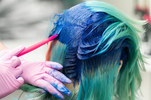 Vista lateral de teñir el cabello en un color único peluquero en guante con pincel rosa mientras aplica azul