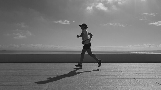 Vista lateral de toda la longitud de la mujer corriendo en el paseo marítimo contra el cielo