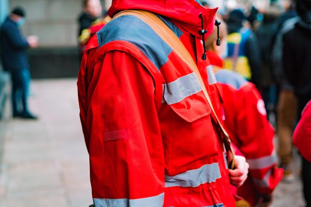 Una vista lateral de un trabajador médico de emergencia en un uniforme rojo de pie en la calle durante la protesta Ambulancia Asistencia Gente Hombre Calle Médico Paramédico Urgencia Primeros auxilios Rescate de pacientes