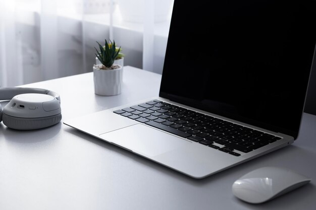 Vista lateral en ultrabook ordenador portátil ratón auriculares de música y plantas en una mesa blanca en la oficina en casa