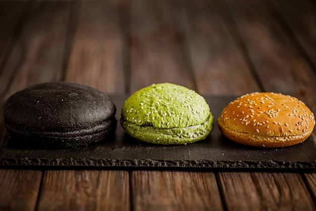 Vista lateral de la variedad de tres bollos de hamburguesa en la mesa de madera Bollos amarillos verdes negros