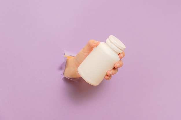 Vista legal em garrafa branca tubo de plástico nas mãos em fundo lila Embalagem para pílulas cápsulas ou suplementos Cosméticos