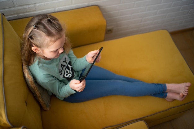 vista ligeramente aérea de una adolescente con ropa informal usando una tableta adicta a jugar