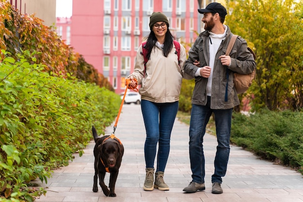 Vista de longitud completa de la joven pareja caminando con su perro en una calle de la ciudad mientras se toman de la mano. Concepto de mascotas y propietarios.