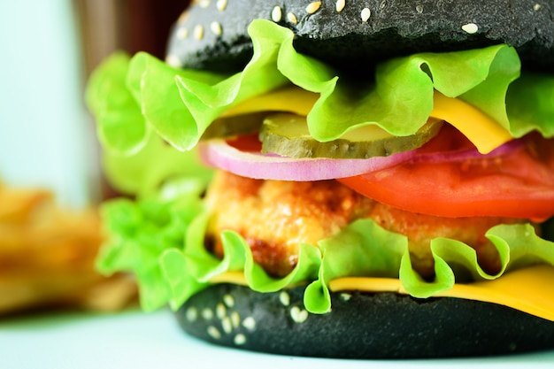 Vista macro do hamburguer preto saboroso com carne, queijo, alface, cebola, tomates no fundo azul.