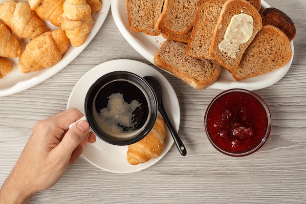 Vista de la mano masculina sosteniendo una taza de café negro en la mesa