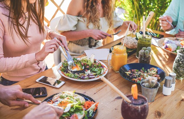 Foto vista de manos de jóvenes comiendo brunch y bebiendo batidos cuenco con pajitas ecológicas en el moderno bar restaurante. estilo de vida saludable, concepto de tendencias alimentarias