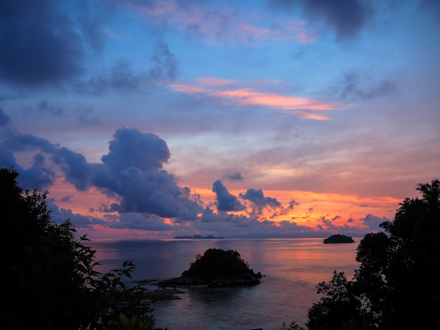 Foto vista del mar de la salida del sol con la pequeña isla y cielo colorido a través del árbol deja silueta
