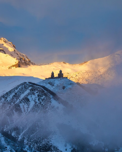 Vista matutina de la iglesia Gergety Trinity y montañas cubiertas de nubes en Kazbegi Georgia