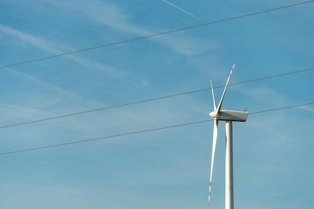 Vista de un molino de viento moderno contra un cielo azul Las palas blancas de la turbina eólica se cierran Fuente de energía renovable Producción de electricidad barata y segura