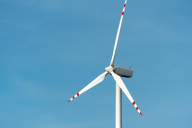 Vista de un molino de viento moderno contra un cielo azul Las palas blancas de la turbina eólica se cierran Fuente de energía renovable Producción de electricidad barata y segura