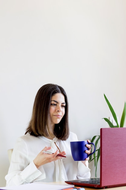 Vista de la mujer casual que trabaja desde su casa con una taza de café en la mano.