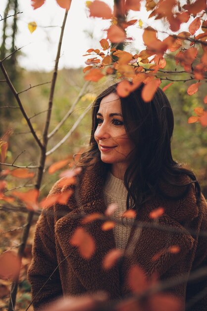 Vista de una mujer morena a través de ramas y hojas en un bosque en otoño