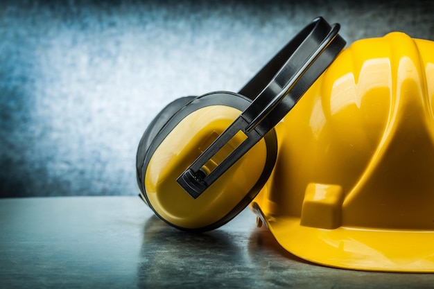 Vista muy cercana construcción casco amarillo y auriculares sobre fondo metálico