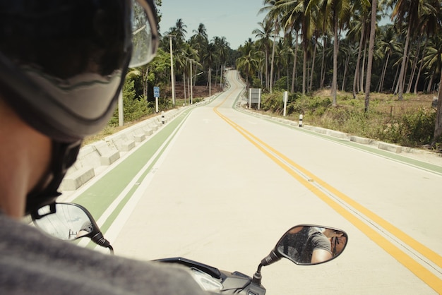 Vista na rodovia do ponto de motorista da scooter. Atrás do turista na estrada na Tailândia, Phangan.