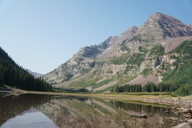 Vista natural de un lago tranquilo y un bosque contra montañas rocosas bajo un día soleado