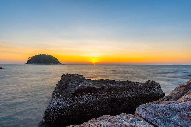 Vista de la naturaleza de la puesta de sol en el mar. Playa de roca y agua de desenfoque de movimiento. Isla o montaña en el mar