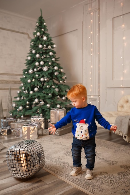 Una vista de un niño ucraniano pelirrojo parado cerca del árbol de Navidad y esperando regalos