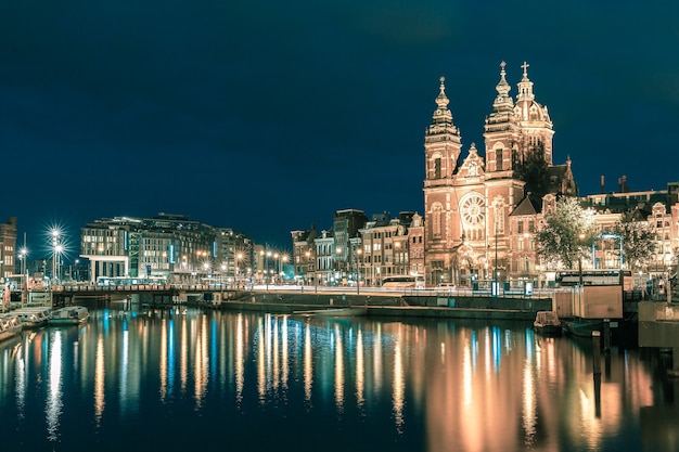 Vista nocturna de la ciudad del canal de Amsterdam y la Basílica de San Nicolás, Holanda, Países Bajos. Larga exposición .. Tonificación en tonos fríos