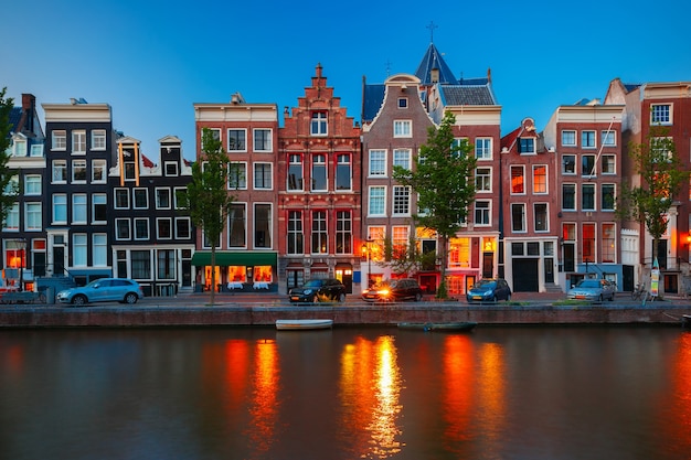 Vista nocturna de la ciudad del canal de Amsterdam, casas y barcos típicos holandeses, Holanda, Países Bajos.