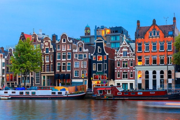 Vista nocturna de la ciudad del canal de Amsterdam, casas y barcos típicos holandeses, Holanda, Países Bajos.