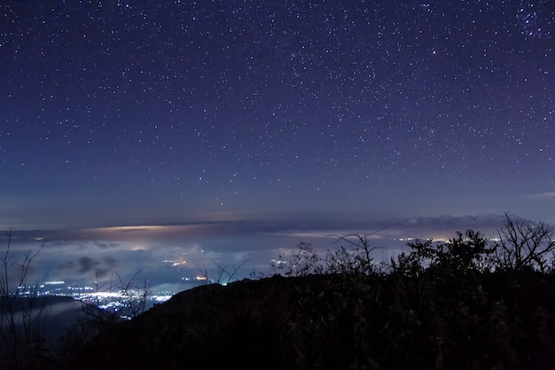 Vista nocturna con estrellas sobre las nubes y la montaña