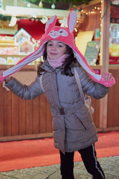 Vista nocturna de una niña sonriente con un sombrero rosa con orejas iluminadas en Navidad en Toledo, España