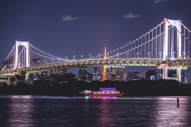 Vista nocturna del puente Rainbow y la torre de Tokio. El crucero se navega en la bahía de Tokio, Odaiba por la noche, Japón.