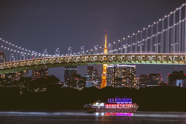 Vista nocturna del puente Rainbow y la torre de Tokio. El crucero se navega en la bahía de Tokio, Odaiba por la noche, Japón.