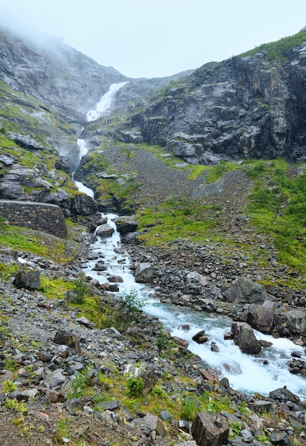 Vista nublada de montaña de verano con cascada en pendiente