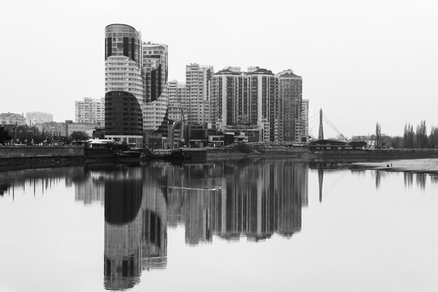 Vista de los nuevos y modernos edificios de apartamentos de varios pisos con reflejo en el agua del río Kuban en una brumosa mañana de otoño Foto en blanco y negro