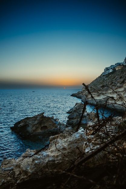 Vista del océano al atardecer con rocas y ramas de árboles enmarcando la escena