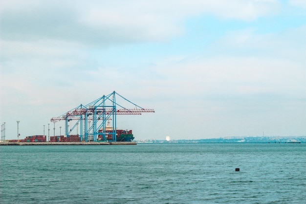 Vista desde la orilla al puerto con grúas y contenedores.