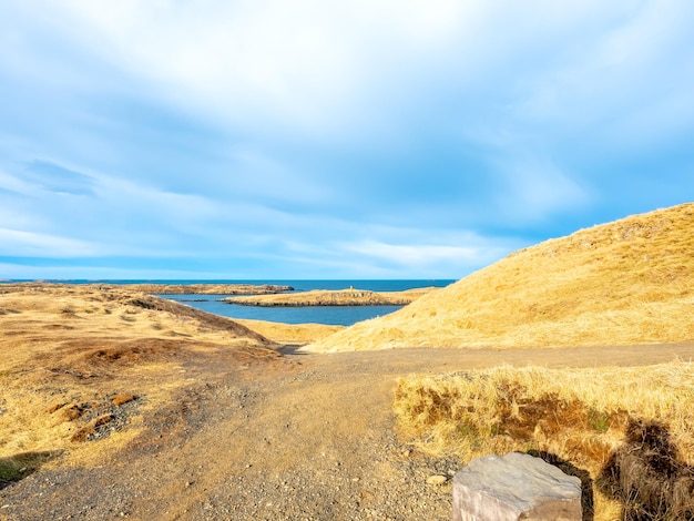 Vista del paisaje marino con montaña bajo un cielo azul nublado desde la colina del faro de Stykissholmur en Islandia