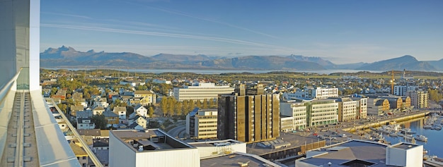 Vista del paisaje urbano de los edificios de la ciudad urbana y la infraestructura con montañas de fondo en el popular destino de viajes al extranjero Centro de la ciudad ocupado y arquitectura urbana y cielo azul en Bodo Noruega