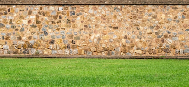 Vista panorámica de la antigua pared de piedra vintage y césped verde en un jardín como diseño paisajístico