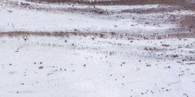 Vista panorámica desde arriba sobre la textura del camino de tierra de grava cubierto de nieve en el bosque