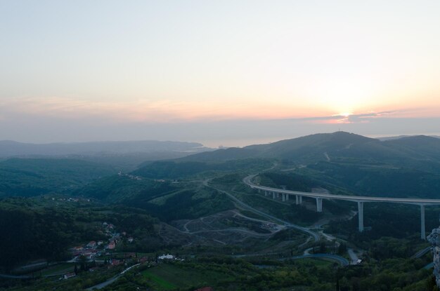 Vista panorâmica. belas colinas verdes, grande ponte contra o céu laranja vermelho, primavera. Da costa da Eslovênia