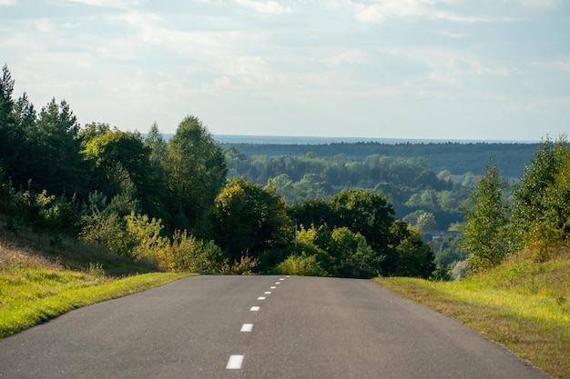 Vista panorámica desde la cima de la colina hasta la carretera y el bosque otoñal en el horizonte Una carretera asfaltada vacía atraviesa una zona montañosa a través de un bosque y un pueblo Espacio vacío para texto