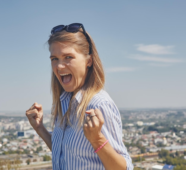 Vista panorámica de una ciudad y una mujer joven de buen humor en primer plano con los brazos apretados