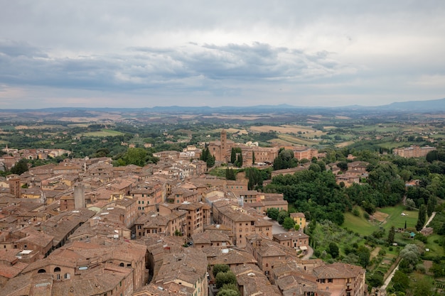 Vista panorámica de la ciudad de Siena con edificios históricos y lejanos campos verdes de Torre del Mangia es una torre en la ciudad. Día soleado de verano y espectacular cielo azul