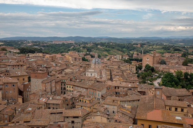 Vista panorâmica da cidade de Siena com edifícios históricos e campos verdes distantes da Torre del Mangia é uma torre na cidade. Dia ensolarado de verão e céu azul dramático