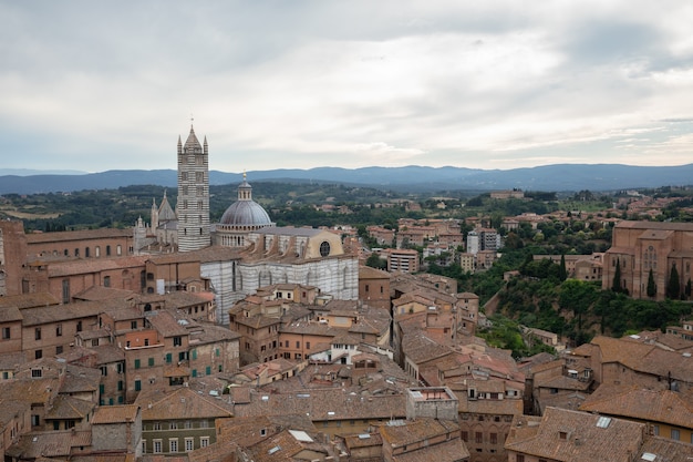 Vista panorâmica da cidade de Siena com edifícios históricos e campos verdes distantes da Torre del Mangia é uma torre na cidade. Dia ensolarado de verão e céu azul dramático