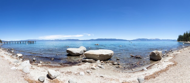 Vista panorâmica da praia rochosa e doca no lago cercado por montanhas