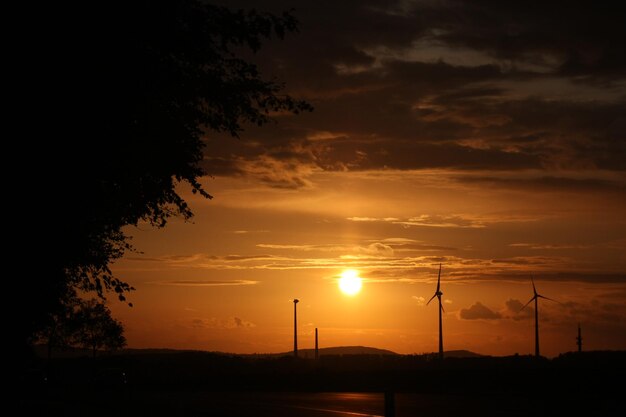 Foto vista panorâmica de silhuetas de árvores e moinhos de vento contra o céu durante o pôr-do-sol