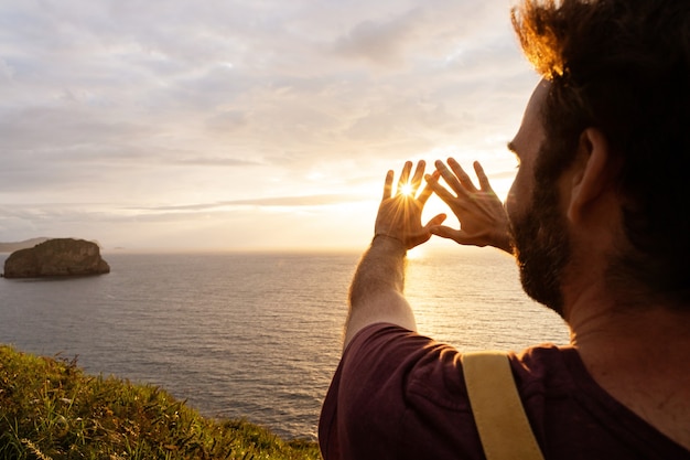 Vista panorâmica do homem irreconhecível ao pôr do sol em um penhasco. visão horizontal do mochileiro viajando ao ar livre com o oceano azul ao fundo.