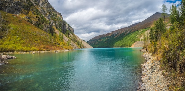 Vista panorâmica do lago de montanha clara na floresta entre os abetos no sol. Cenário brilhante com belo lago turquesa no contexto das montanhas cobertas de neve. Lago Shavlin inferior.