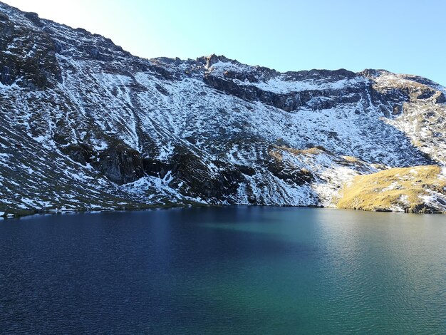 Foto vista panorâmica do lago por montanhas cobertas de neve contra um céu azul claro