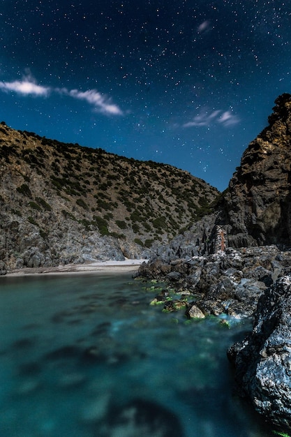 Vista panorâmica do lago por rochas contra o campo de estrelas à noite