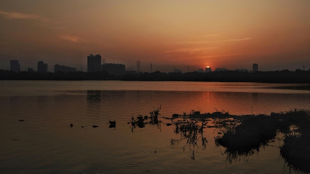 Foto vista panorâmica do lago por silhuetas de edifícios contra o céu durante o pôr-do-sol